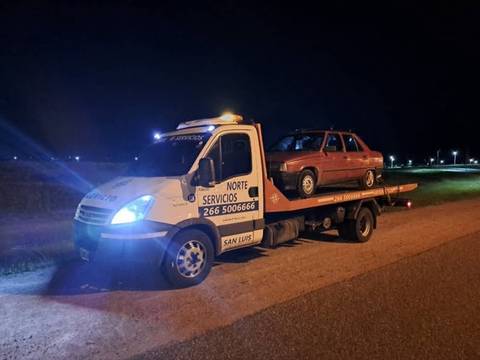 Grúa de la flota de noche, con las balizas encendidas y un auto cargado